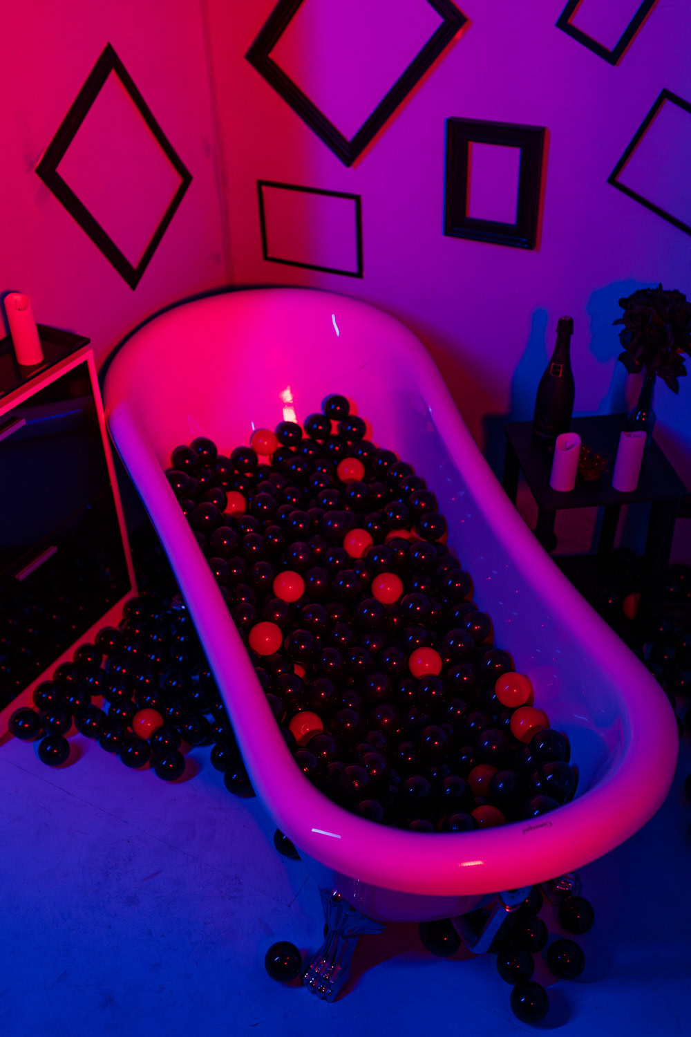 Das Bild zeigt eine moderne Badewanne, gefüllt mit schwarzen und orangefarbenen Bällen, umgeben von farbenfrohen Lichtern in lila und blau, die eine entspannte Atmosphäre schaffen. Diese kreative Kulisse eignet sich hervorragend für Boudoir-Fotografie in Ingolstadt und Pfaffenhofen, die individuelle und stilvolle Porträts zu schätzen wissen.
