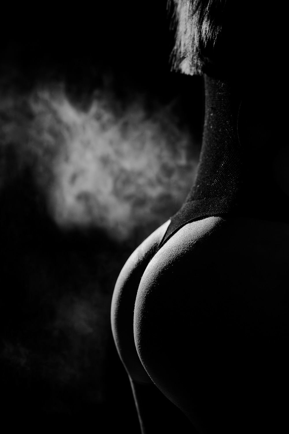 Das Bild zeigt eine stilvolle Boudoir-Fotografie in Schwarz-Weiß, die durch kontrastreiche Licht- und Schattenverhältnisse sowie eine mysteriöse Nebelkulisse besticht. Diese Kunstform ist besonders in Ingolstadt und Pfaffenhofen beliebt, da sie die Sinnlichkeit und Eleganz der Portraitierten eindrucksvoll einfängt.