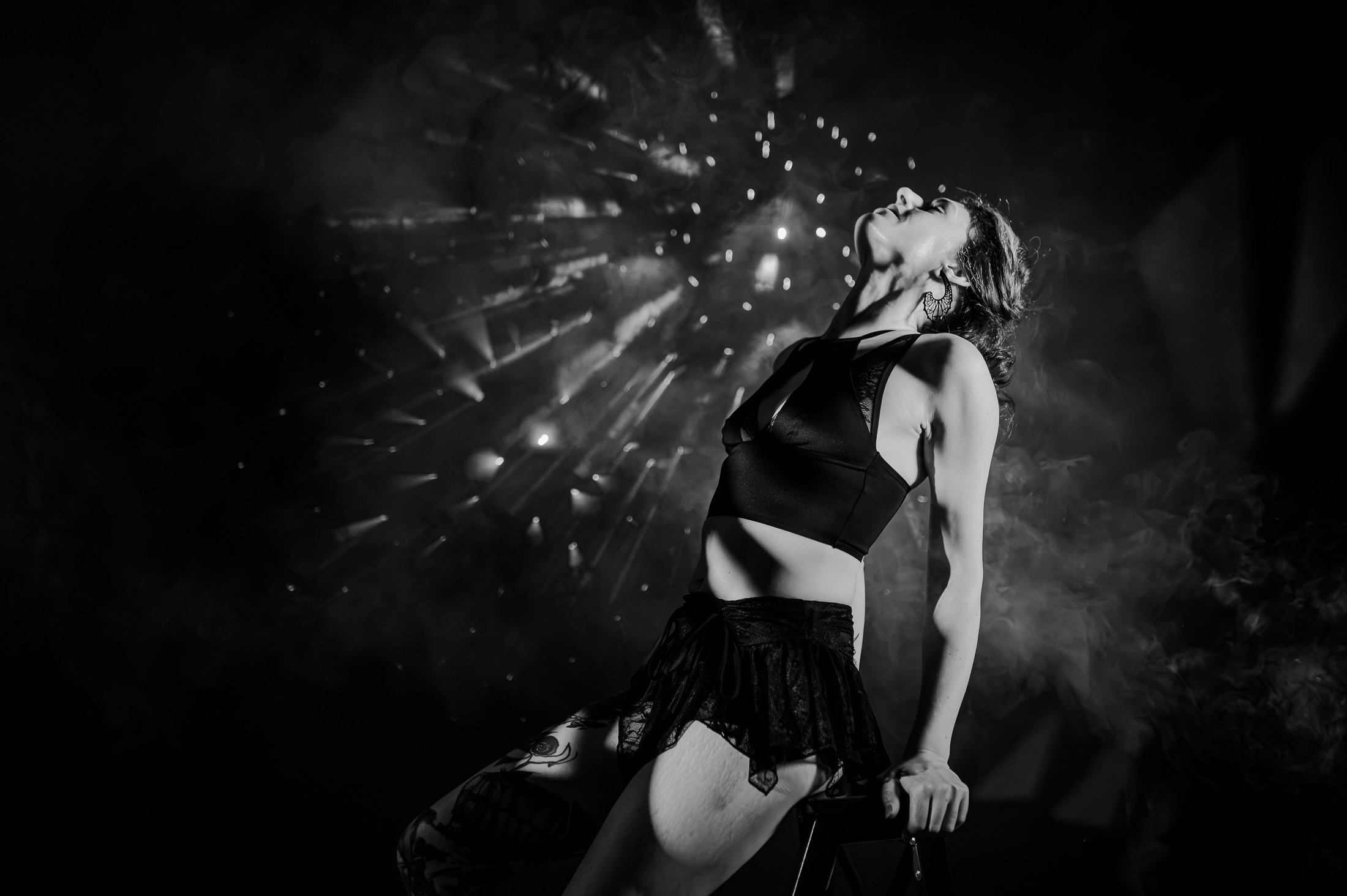Das Bild zeigt eine dynamische schwarz-weiße Boudoir-Fotografie, in der eine Person in einem sinnlichen Pose vor einem dramatikreichen, beleuchteten Hintergrund präsentiert wird. Die kreative Inszenierung kombiniert Kunst und Ästhetik, ideal für Fotografien aus Ingolstadt und Pfaffenhofen.